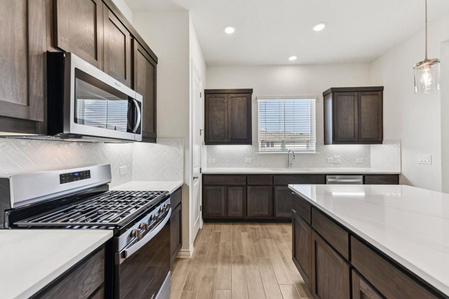 Kitchen with appliances with stainless steel finishes, dark brown cabinets, tasteful backsplash, light wood finished floors, and recessed lighting Kitchen with appliances with stainless steel finishes, dark brown cabinets, tasteful backsplash, light wood finished floors, and recessed lighting