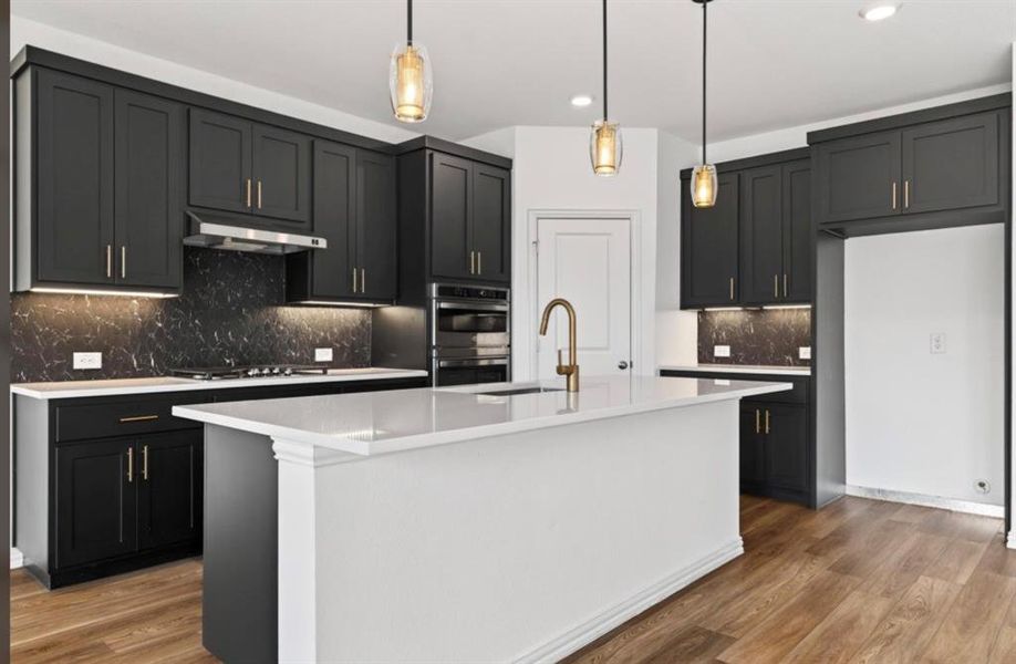 Kitchen with backsplash, dark cabinets, hanging light fixtures, light wood-style flooring, and a kitchen island with sink