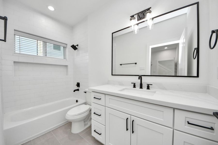 This modern 3rd bathroom features sleek black fixtures, a large vanity with ample storage, and a spacious tub. The room is bright with a clean, white tile design and a large mirror, enhancing the open feel.
