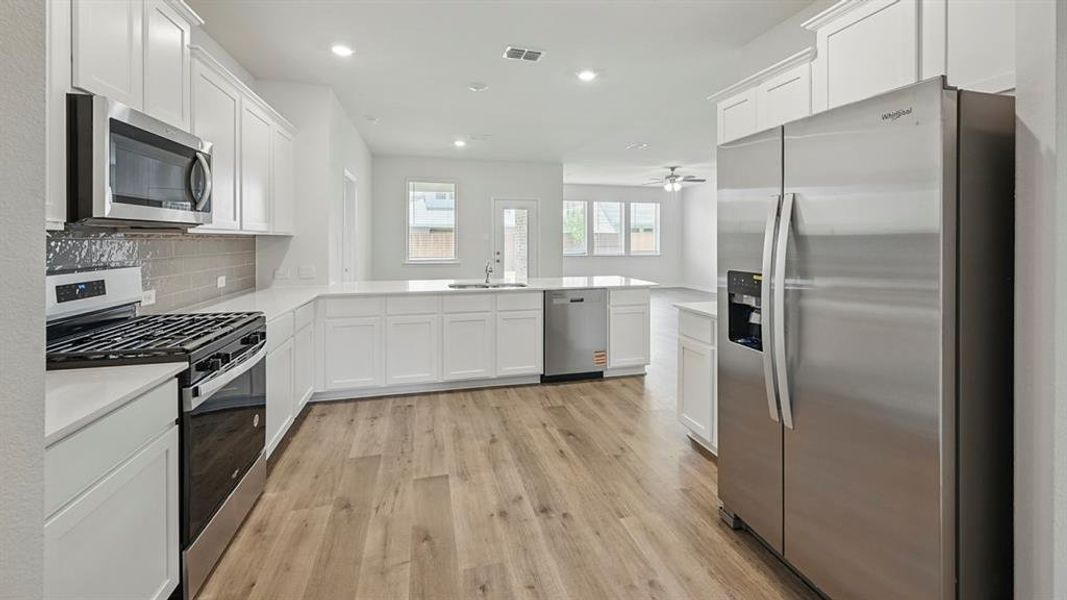 Kitchen with appliances with stainless steel finishes, white cabinetry, open floor plan, light wood finished floors, and a peninsula Kitchen with appliances with stainless steel finishes, white cabinetry, open floor plan, light wood finished floors, and a peninsula