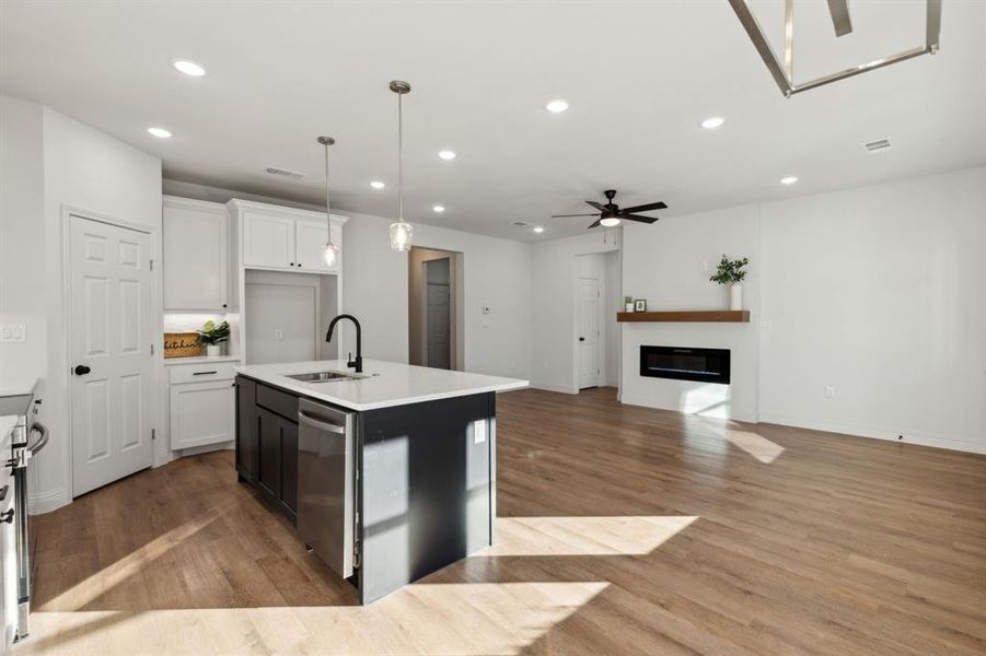 Kitchen featuring ceiling fan, sink, a center island with sink, dishwasher, and white cabinets