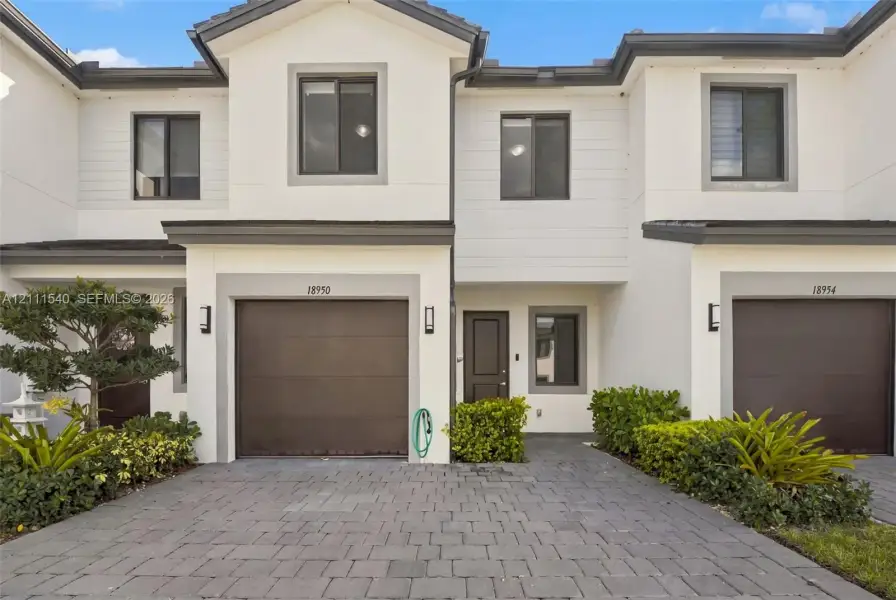 Two-story exterior featuring white stucco siding, gray trim, paved driveway, single-car garage, and manicured landscaping