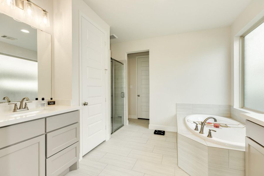 Primary bathroom features exquisite tile flooring, double vanities complemented by excellent lighting, a deep soaking tub positioned beside a frosted window for privacy, and a spacious glass walk-in shower. Primary bathroom features exquisite tile flooring, double vanities complemented by excellent lighting, a deep soaking tub positioned beside a frosted window for privacy, and a spacious glass walk-in shower.