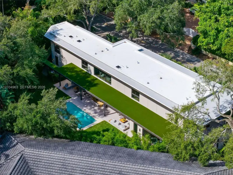 Modern residence featuring a flat roof with integrated skylights, a sprawling covered terrace with an artificial turf canopy, and a private swimming pool set within a manicured backyard