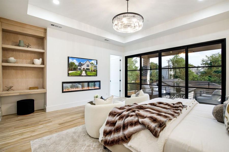 Expansive sliding glass doors with black framing, wood-finish flooring, a contemporary linear electric fireplace, built-in shelving, and a modern chandelier Expansive sliding glass doors with black framing, wood-finish flooring, a contemporary linear electric fireplace, built-in shelving, and a modern chandelier