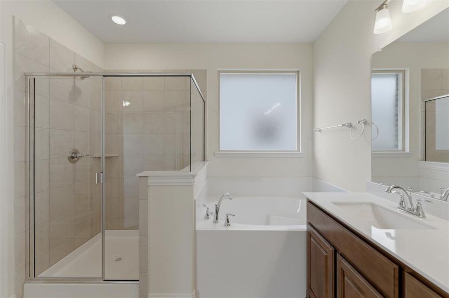Bathroom featuring a glass-enclosed shower with tile surround, a built-in bathtub with chrome fixtures, a single vanity with a white countertop and undermount sink, a framed mirror, and a privacy window