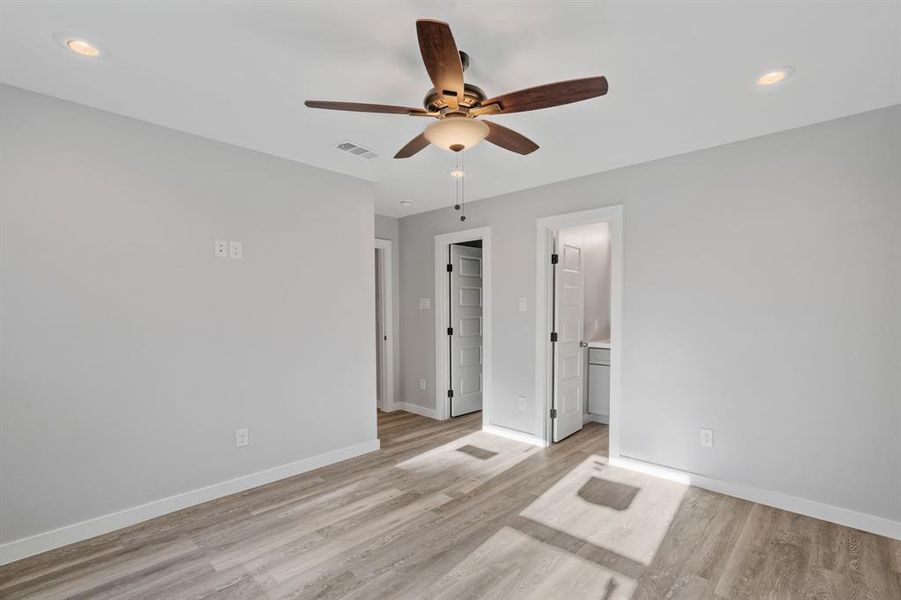 Unfurnished bedroom featuring light hardwood / wood-style floors, a spacious closet, ensuite bathroom, and ceiling fan