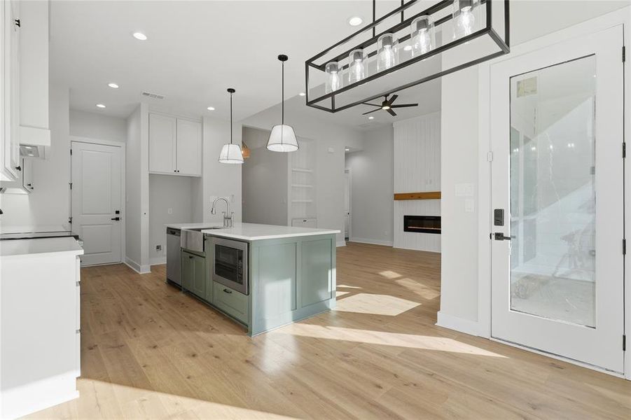 Open-concept kitchen and living area featuring light wood-finish flooring, a kitchen island with an integrated farmhouse sink, white countertops, and recessed lighting Open-concept kitchen and living area featuring light wood-finish flooring, a kitchen island with an integrated farmhouse sink, white countertops, and recessed lighting