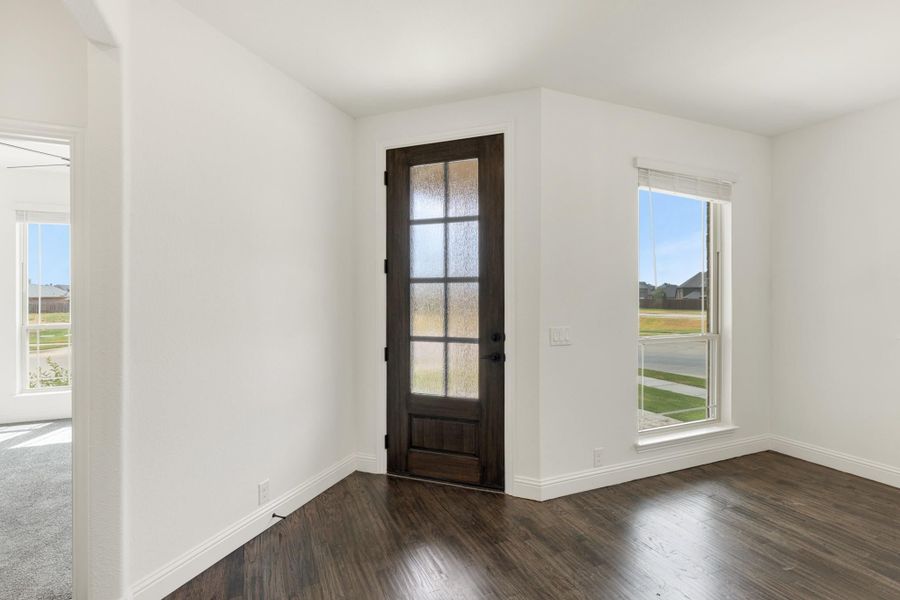 Empty room with dark hardwood floors, white walls, and a dark wood glass-panel exterior door with side window