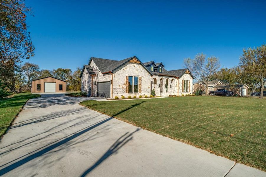 View of front facade featuring stone siding, a detached garage, a front lawn, and an outdoor structure View of front facade featuring stone siding, a detached garage, a front lawn, and an outdoor structure