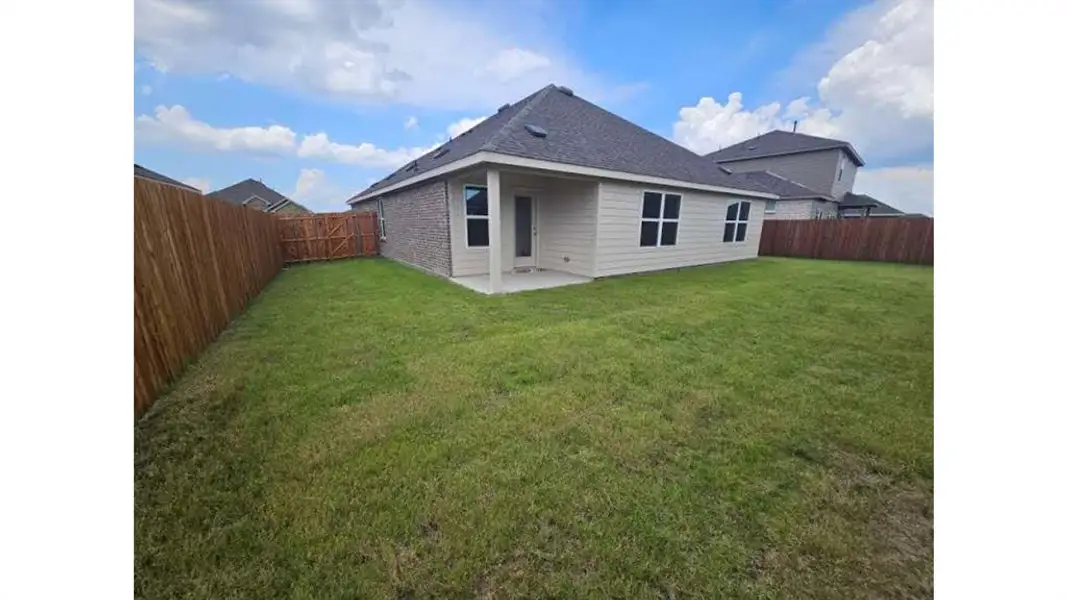 Spacious rear yard with a manicured lawn, full privacy fencing, and a concrete patio