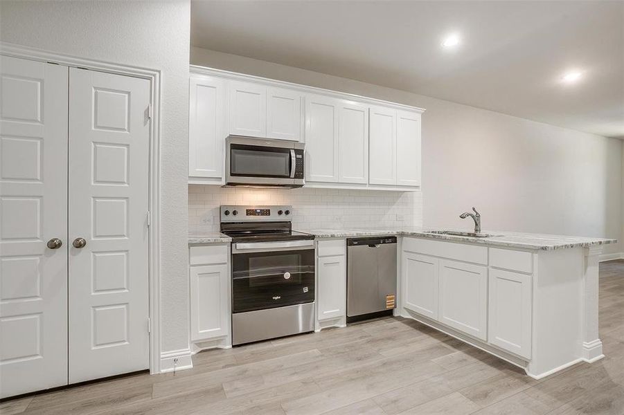 Kitchen with stainless steel appliances, tasteful backsplash, a peninsula, white cabinetry, and light wood-style floors