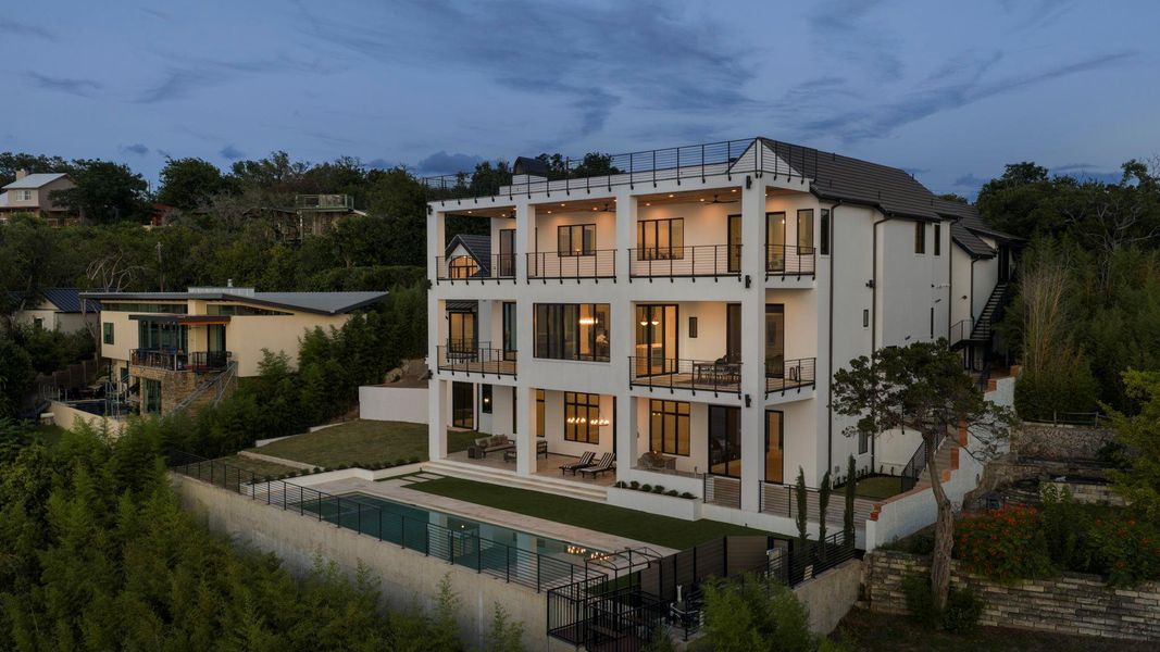 Multi-story architecture with tiered balconies overlooks a secluded backyard oasis and sparkling pool. Multi-story architecture with tiered balconies overlooks a secluded backyard oasis and sparkling pool.