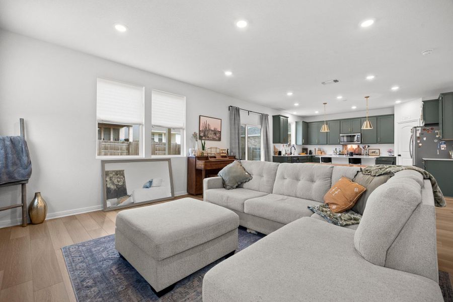 Open-concept living area featuring light wood-finish flooring, recessed lighting, and a modern kitchen with green cabinetry and pendant lights