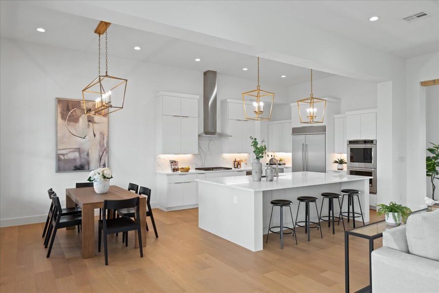 Kitchen with appliances with stainless steel finishes, wall chimney exhaust hood, a chandelier, a breakfast bar area, and light countertops