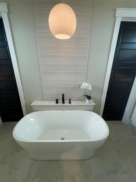 Freestanding soaking tub with matte black fixtures, set against a tiled accent wall