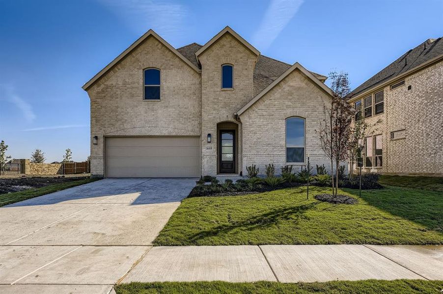 French provincial home featuring brick siding, concrete driveway, a front yard, and an attached garage