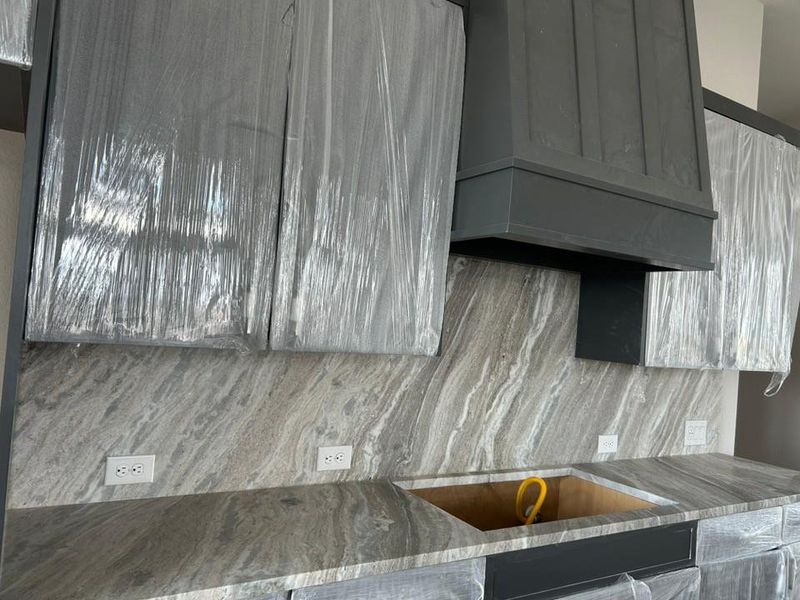 Kitchen view of decorative backsplash, premium range hood, and black electric cooktop