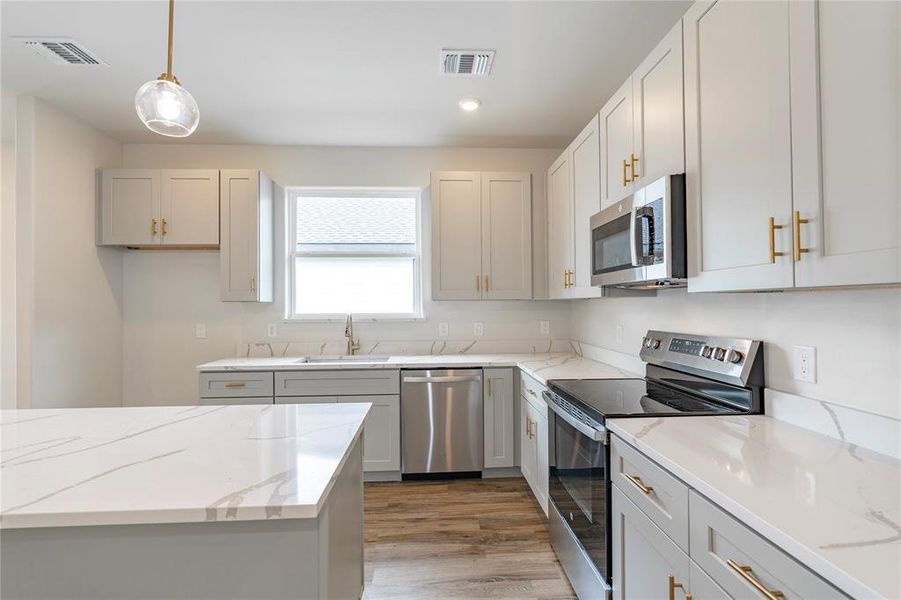 Kitchen featuring hanging light fixtures, appliances with stainless steel finishes, light stone countertops, sink, and wood-type flooring