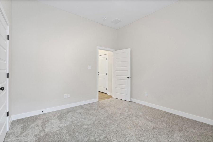 Carpeted room featuring a neutral wall palette, white baseboards, and white paneled doors with black hardware Carpeted room featuring a neutral wall palette, white baseboards, and white paneled doors with black hardware