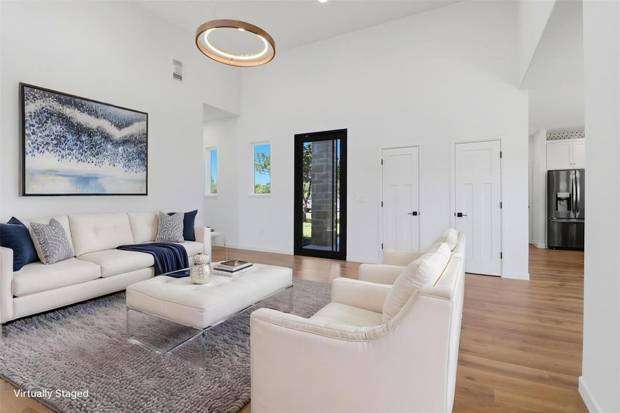 Open concept living area featuring vaulted ceilings, wood-finish flooring, a contemporary chandelier, a full-light entry door with dark trim, and crisp white walls Open concept living area featuring vaulted ceilings, wood-finish flooring, a contemporary chandelier, a full-light entry door with dark trim, and crisp white walls