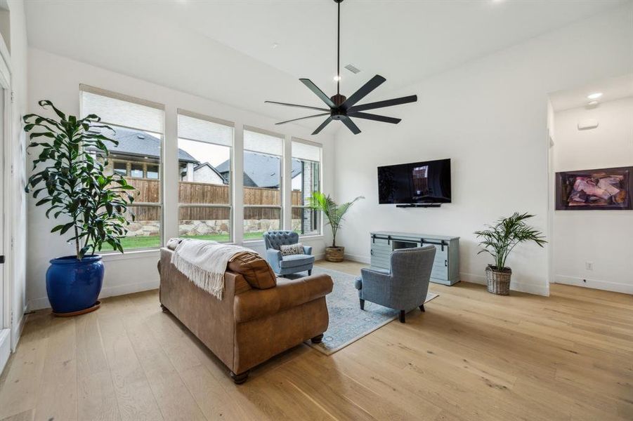 Living room featuring light wood-type flooring, a ceiling fan, plenty of natural light, and baseboards