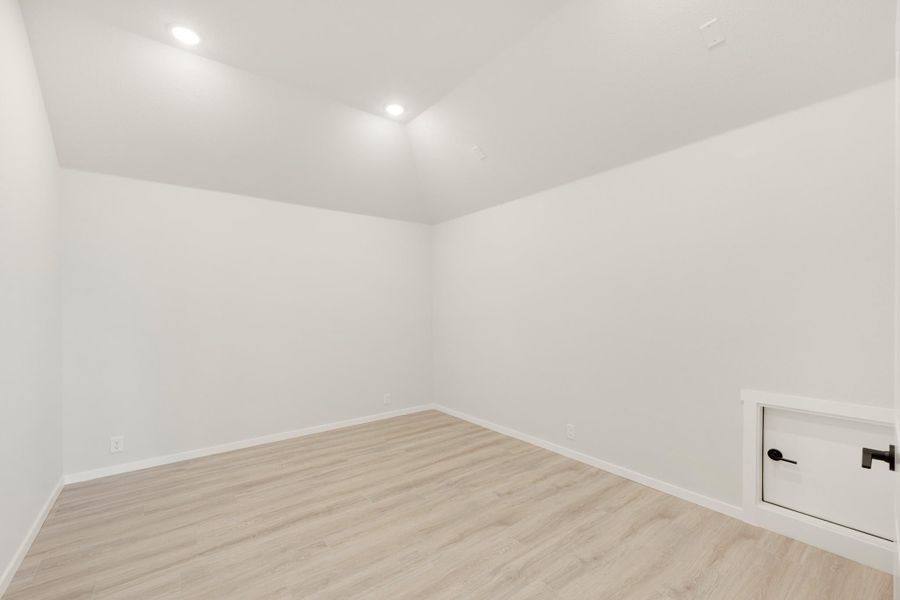 Empty room with white walls, light wood floors, recessed lighting, and a small built-in cabinet with black hardware.