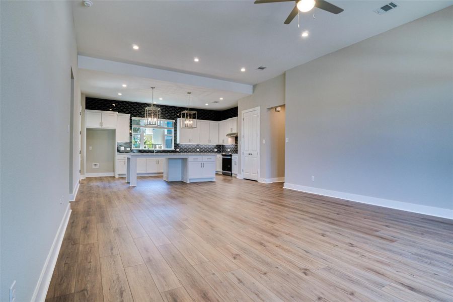 Kitchen with a center island, white cabinets, light wood-type flooring, pendant lighting, and ceiling fan with notable chandelier