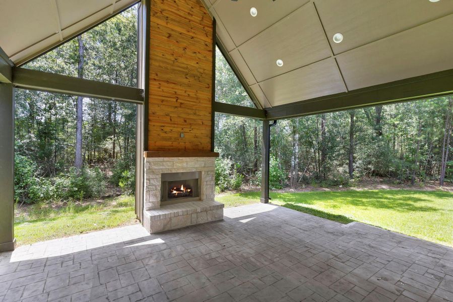 This outdoor space features a covered patio with a vaulted ceiling, built-in lighting, and a cozy fireplace. It opens to a lush, wooded backdrop, providing a serene and private views. Ideal for relaxation or entertaining.
