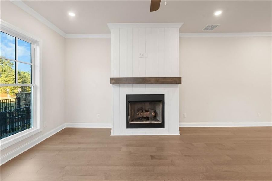 Unfurnished living room with wood finished floors, crown molding, a large fireplace, ceiling fan, and recessed lighting