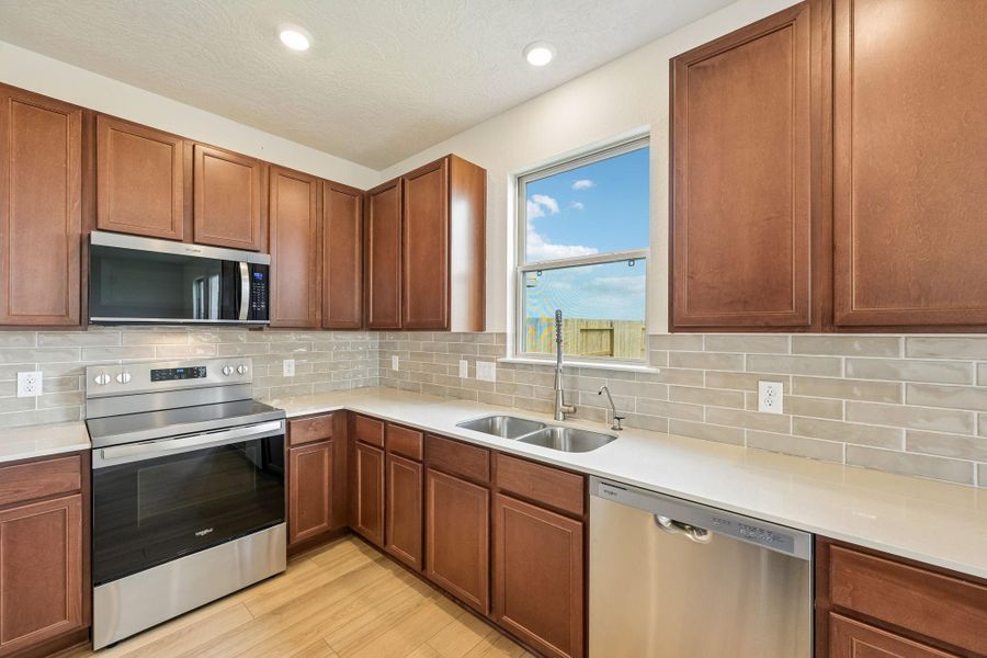 Bright and airy kitchen workspace featuring a classic double-bowl stainless steel sink situated perfectly beneath a sunlit window. Kitchen comes equipped with stainless steel Whirlpool appliances.