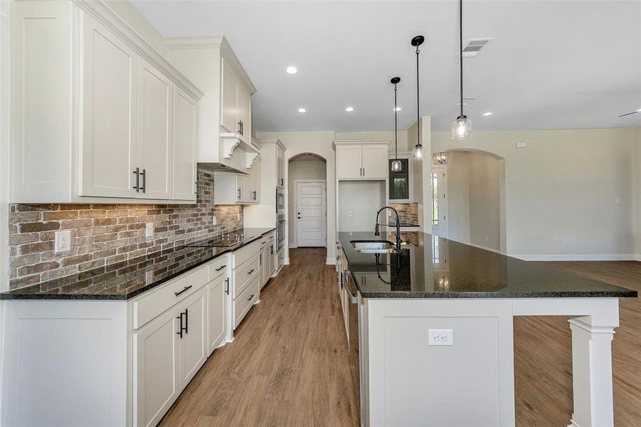 Kitchen with backsplash, decorative light fixtures, light wood-type flooring, sink, and a kitchen island with sink