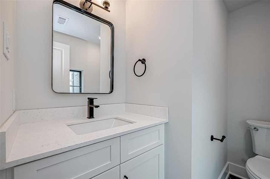 This half bathroom features a modern design with a sleek white vanity, black fixtures, and a large mirror. The countertop is light-colored with a minimalist sink, and there's a toilet visible, creating a clean and stylish look.