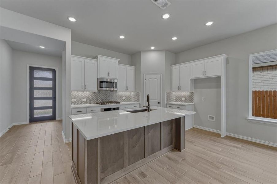 Modern kitchen featuring a central island with a sink, quartz countertops, white cabinetry, and stainless steel appliances