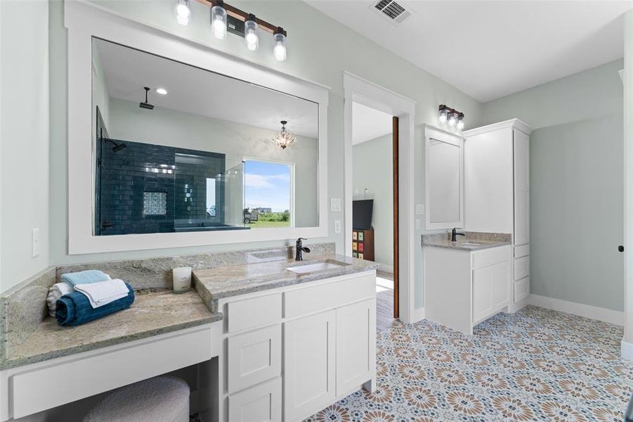 Dual vanity bathroom featuring patterned floor tiling, white cabinetry, stone countertops, and a built-in shower with dark subway tile