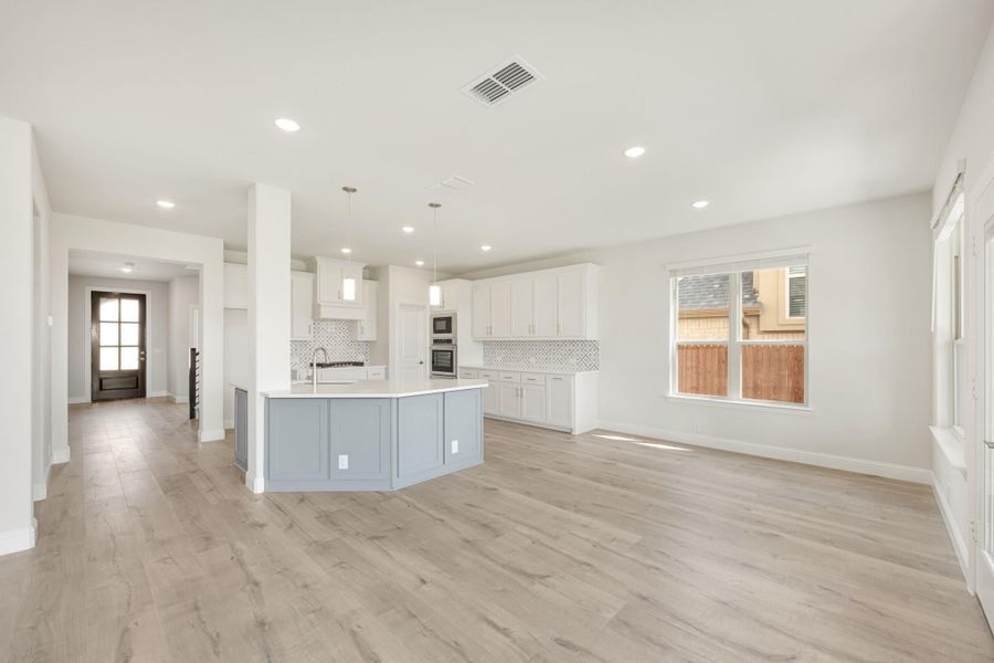 Open-concept kitchen and living area with white cabinets, gray island, tile backsplash, and light wood floors