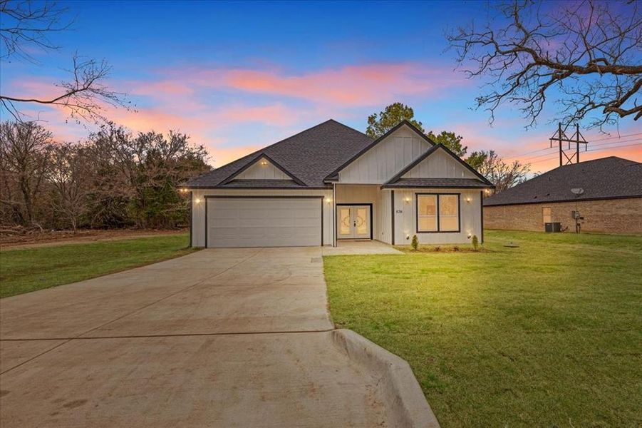 Modern inspired farmhouse featuring an attached garage, concrete driveway, a shingled roof, and a front yard