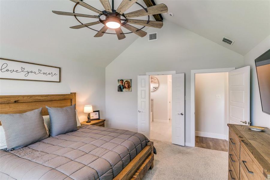 Primary bedroom with light carpet, ceiling fan, and high vaulted ceiling