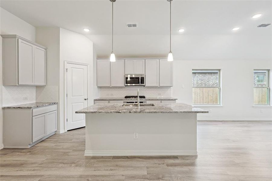 Kitchen featuring backsplash, light hardwood / wood-style floors, a center island with sink, and pendant lighting