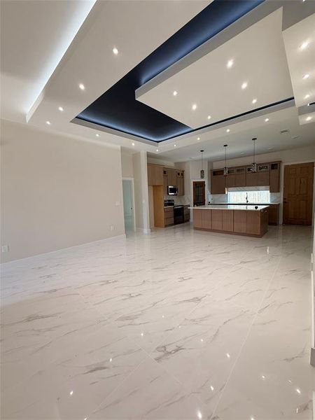 Unfurnished living room with a tray ceiling, recessed lighting, light marble finish flooring, and baseboards