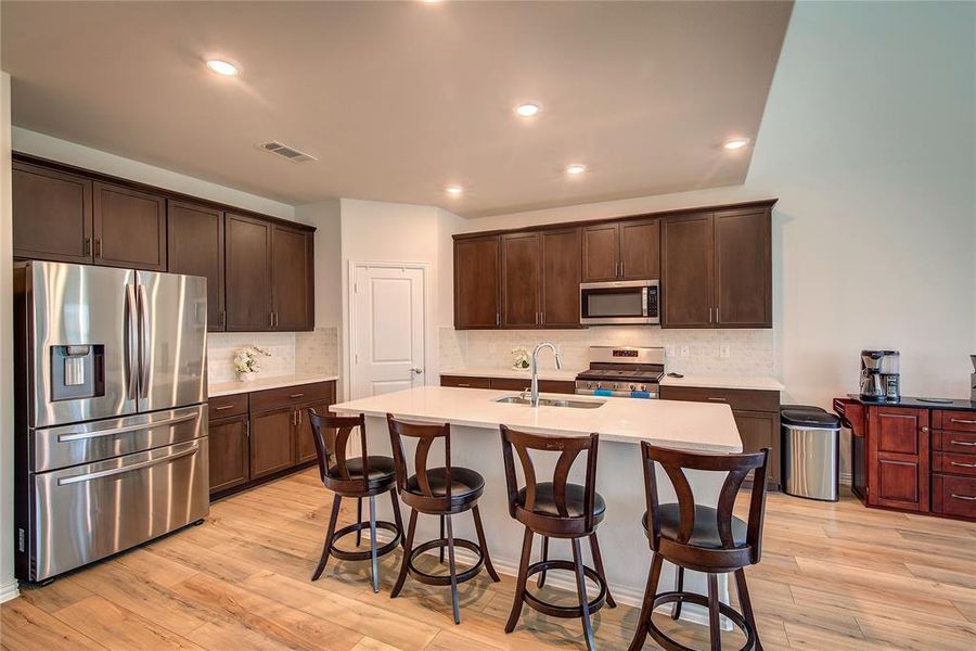 Kitchen featuring tasteful backsplash, stainless steel appliances, sink, light hardwood / wood-style flooring, and an island with sink