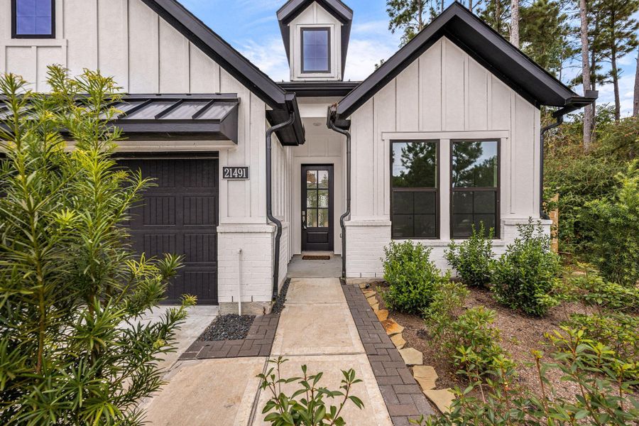 Charming modern farmhouse with a welcoming front entrance, featuring board-and-batten siding, a sleek black door, and lush landscaping.