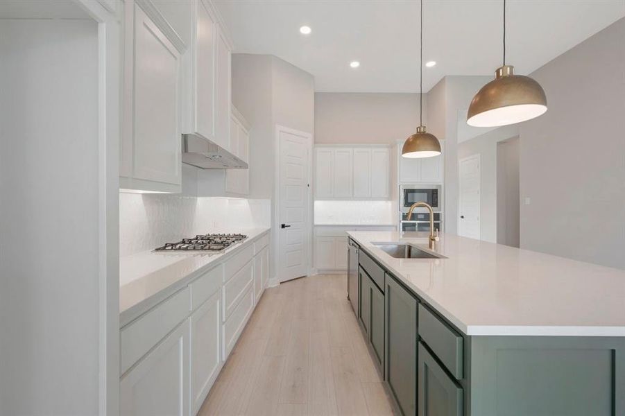 Modern kitchen featuring a large island with a stainless steel sink and gold-tone faucet, white upper and lower cabinetry, a gas cooktop with a stainless steel range hood, and light wood-finish flooring