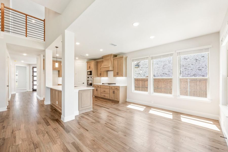 Open-concept living area and kitchen with light wood cabinets, hardwood floors, and second-floor loft railing visible above. Open-concept living area and kitchen with light wood cabinets, hardwood floors, and second-floor loft railing visible above.