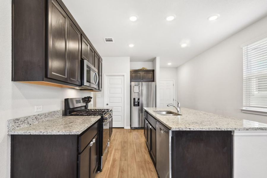 A contemporary kitchen features dark cabinetry, light granite countertops, and modern stainless steel appliances. A contemporary kitchen features dark cabinetry, light granite countertops, and modern stainless steel appliances.