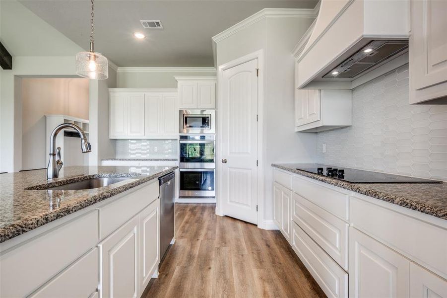 Kitchen with appliances with stainless steel finishes, light hardwood / wood-style flooring, backsplash, and custom exhaust hood