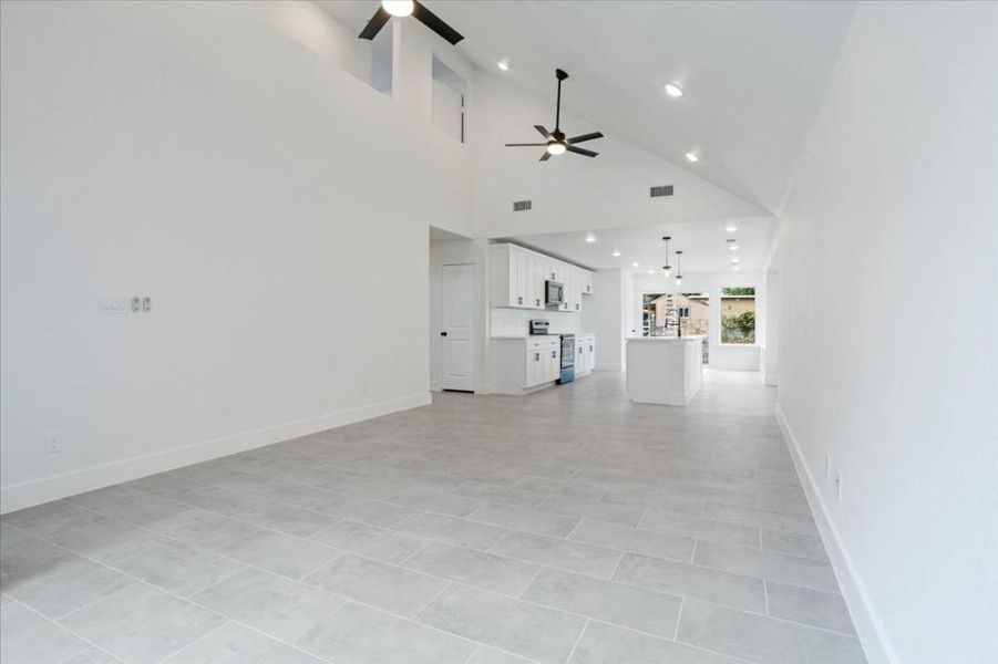 Unfurnished living room with high vaulted ceiling, light tile patterned floors, and ceiling fan