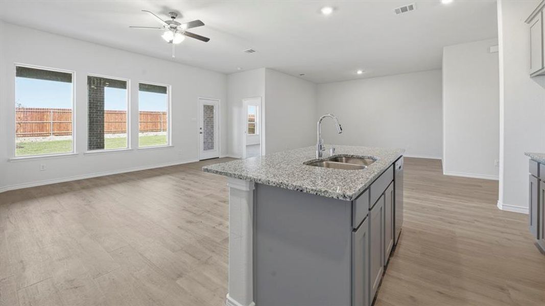 Kitchen with open floor plan, light stone counters, gray cabinetry, light wood-style flooring, and recessed lighting Kitchen with open floor plan, light stone counters, gray cabinetry, light wood-style flooring, and recessed lighting