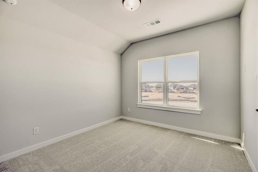 Carpeted spare room featuring baseboards and vaulted ceiling