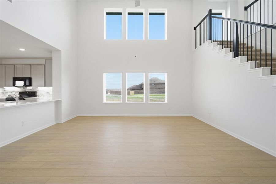 Unfurnished living room featuring plenty of natural light, light wood-type flooring, a ceiling fan, recessed lighting, and a high ceiling
